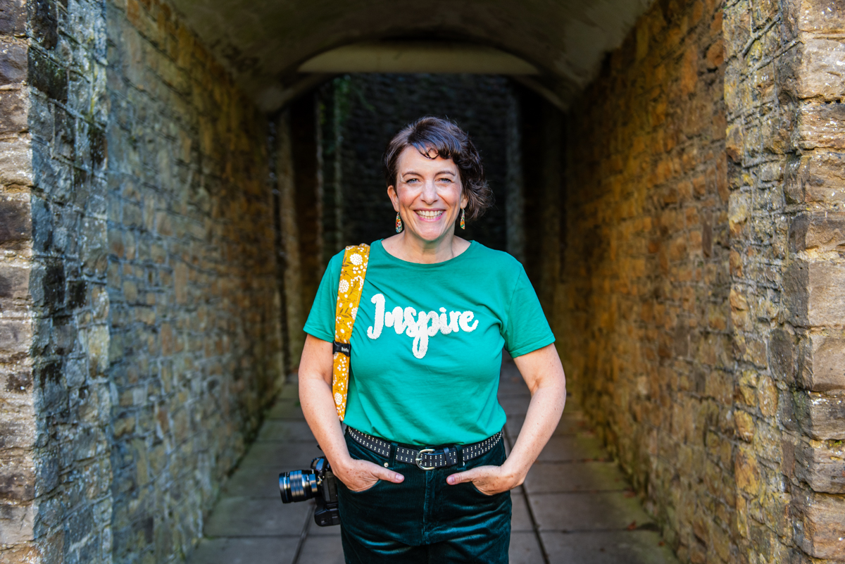 photo of Kerry Harrison with her camera, smiling with a t-shirt that says inspire